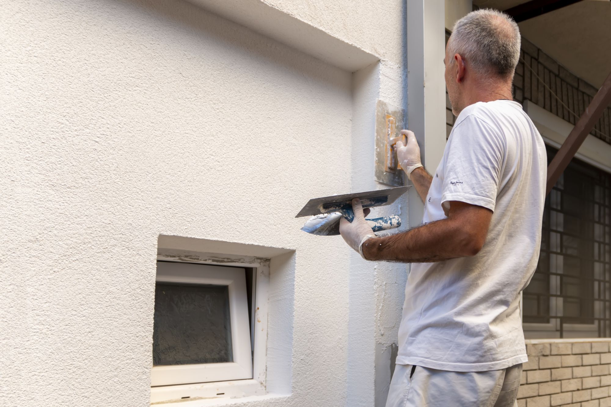 Construction worker applying final decorative facade plaster paste. Home renovation.
